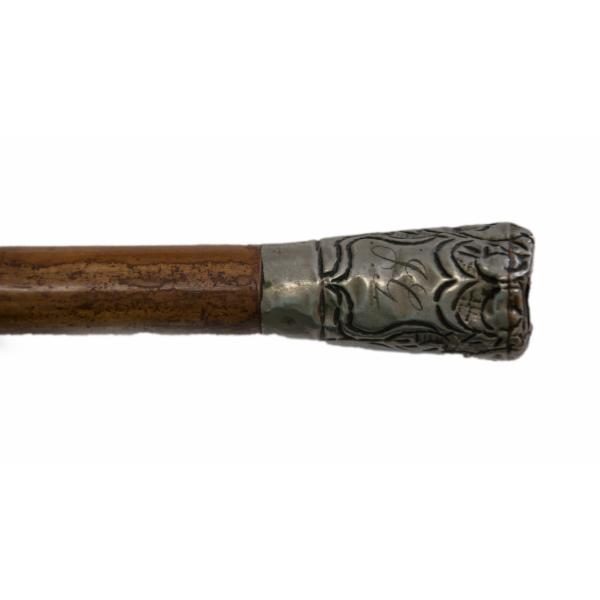 A walking cane made from maple-coloured malacca wood and a brass handle with curved lines etched into it. 