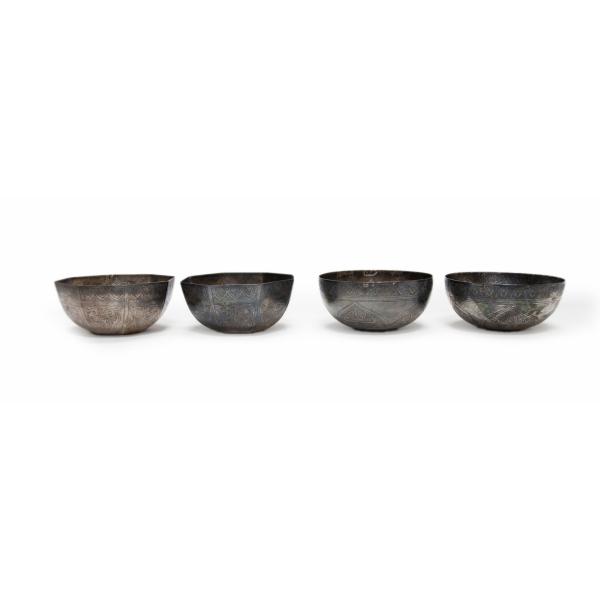 Front side of the set of four silver finger bowls. The two on the left have octagonal sides and the two on the right have smooth sides. They are silver in colour and have detailed patterns inscribed on them.  