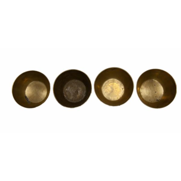 Interior view of four brass finger bowls with flared sides and flat bottoms.  
