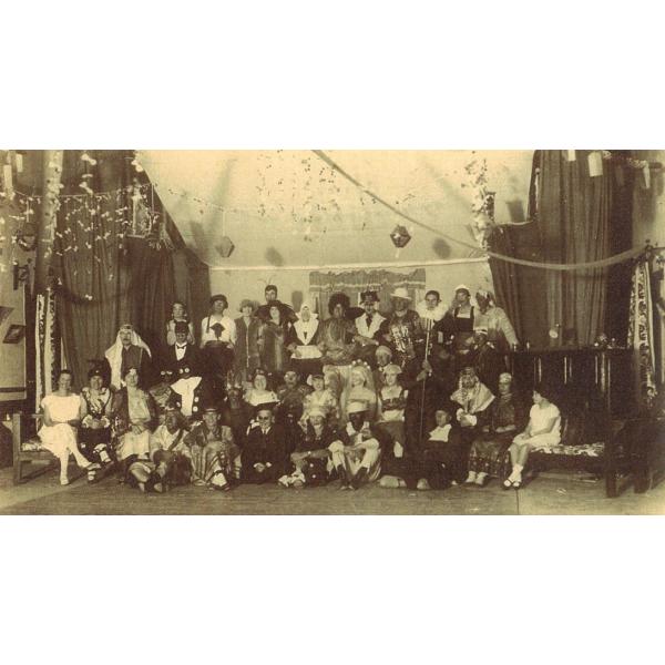  A group of people inside a room with curtains along the walls. They are dressed up in costumes and there are decorations hanging from the ceiling. 