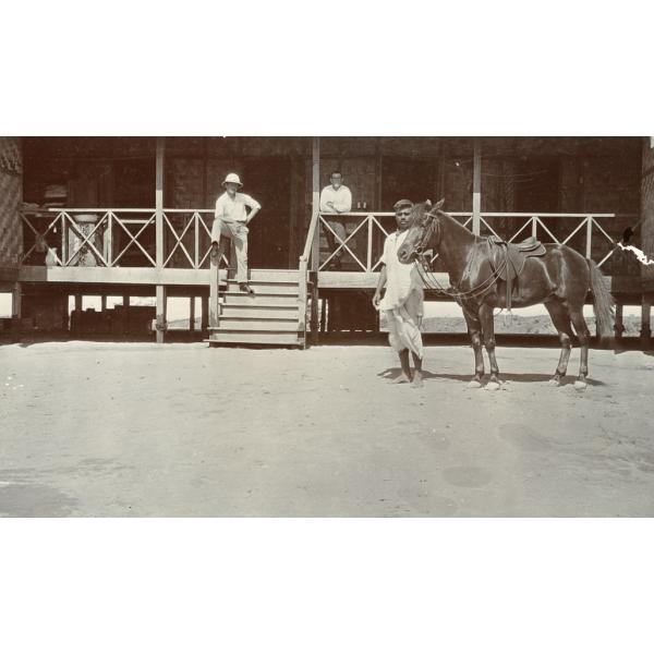 Photograph showing William Gillespie and Albert Gibson on a verandah in Burma. There is a local man with a horse in the front of the image. 