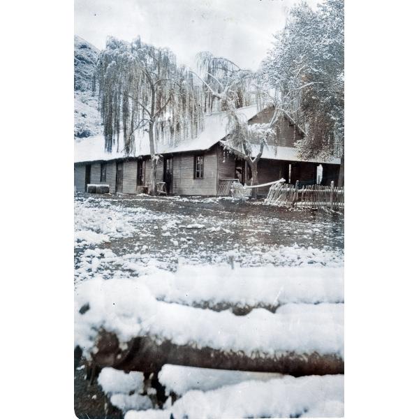 Photo d'un bâtiment avec un porche et un toit en pointe. Il y a de la neige sur le sol devant, sur les arbres autour du bâtiment et sur la colline à l’arrière. 