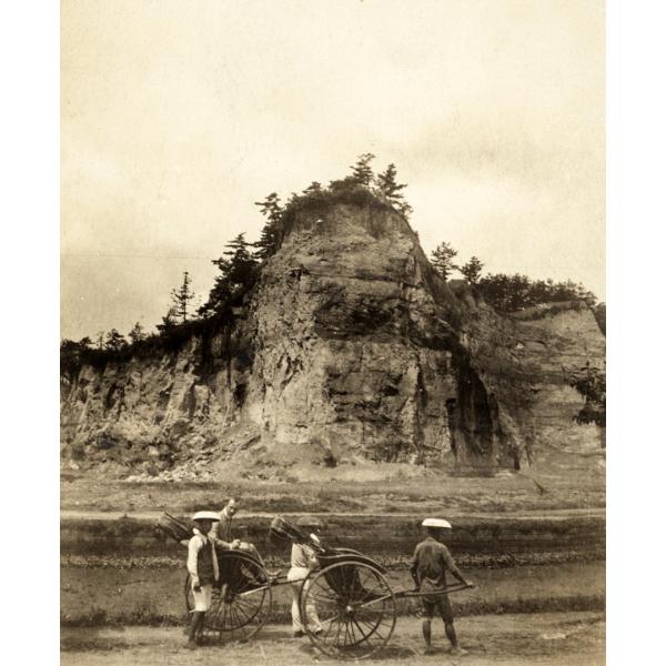 Une photo de quatre personnes avec deux pousse-pousse. Elles se tiennent debout sur une route devant une haute falaise avec des arbres en haut de celle-ci.