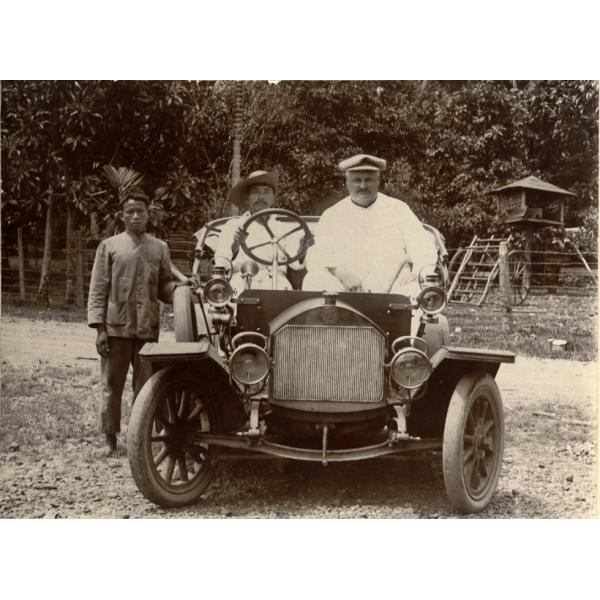 William McRae assis dans une voiture avec un homme de la région au volant. Un autre homme se tient sur le côté.  