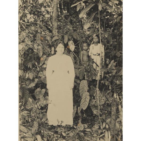 Mrs. McRae wearing a white dress, standing in the jungle with two native children in the background. 