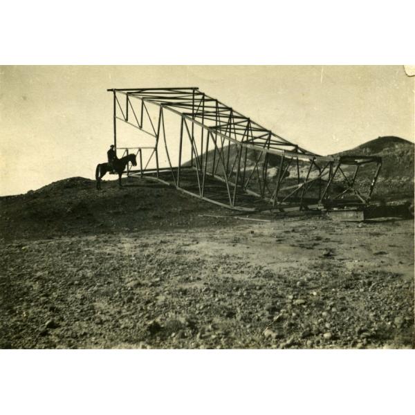  A photo of a man on a horse looking at a steel derrick lying on its side in the dirt.