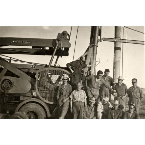 A photo of eleven men in front of a drilling machine with the words "Walker Neer" on it. They are wearing work clothes.