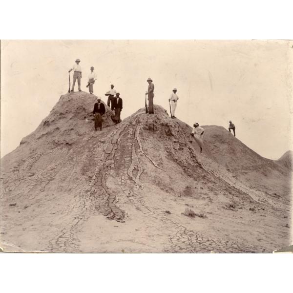 A photo of nine men standing on top of a dirt hill. Four are holding rifles.