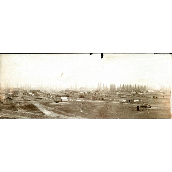 A photo of an oil field with dozens of oil rigs in the background and wooden houses in the foreground. 