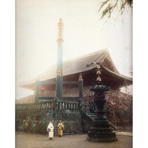 A photo of two Japanese people in traditional clothing, standing in front of a temple. There are cherry blossoms in bloom behind a stone wall and to the right of the image. The photo has been tinted with pinks, yellows, blues, and greens.  