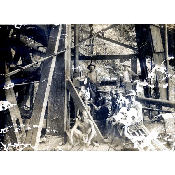 Two International Drillers standing behind six seated labourers inside of an oil rig. There are metal and wood beams around them.