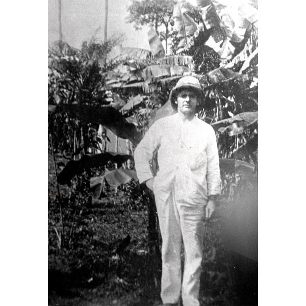 Henry Gregory standing in front of a trees. He is wearing a white suit and pith helmet. 