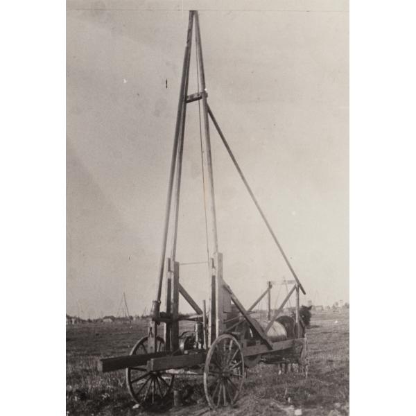 Une machine de trempage de pétrole brut sur une charrette à quatre roues tirée par un cheval. Il y a trois poteaux principaux et un poteau de soutien qui descend vers le cheval. 