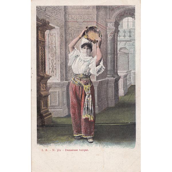 Front of postcard showing a coloured photograph of a Turkish dancer. She is wearing a white shirt and red skirt, and holding a tambourine above her head. 