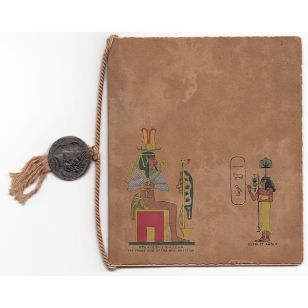Front cover of the Christmas photo-booklet with art in an ancient Egyptian style. There is a piece of string with a medallion and tassel on the right side.