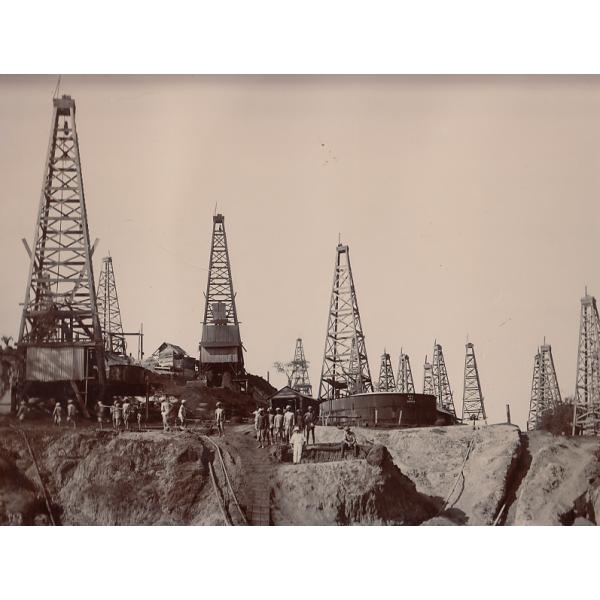 Oil field in Myanmar with many derricks, and local labourers scattered around the scene.