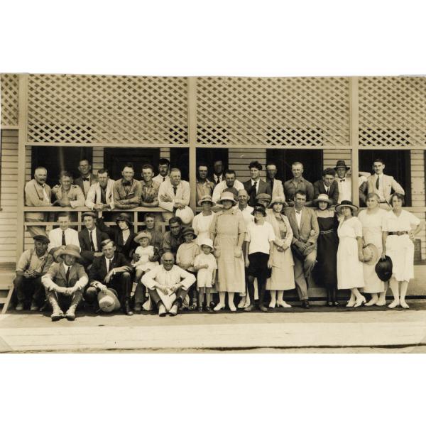Un groupe de foreurs internationaux et leur famille à l’extérieur d’un bâtiment avec ouvrage à claire-voie sur la galerie. Les hommes portent des complets et les femmes sont vêtues de robes.