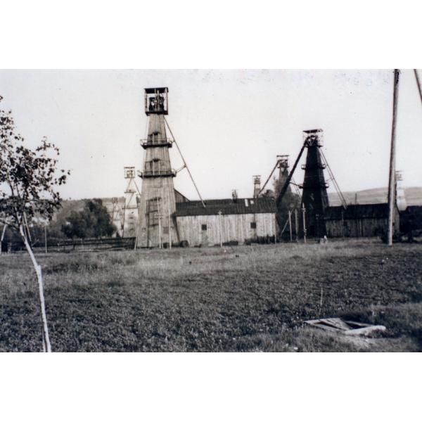 A photo showing eight oil rigs in a Polish oil field. The rigs are covered in wood. There are hills in behind the rigs. 