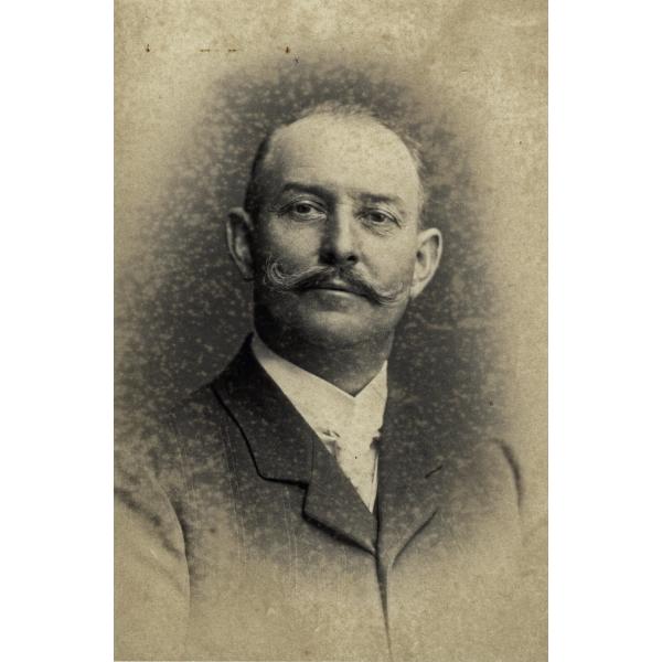 A portrait photo of Jacob Perkins. He has a curled mustache and is wearing a dark jacket over a white-collared shirt. 