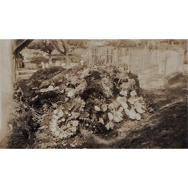 A photo of a mound of earth covered in flowers in a cemetery. There are tombstones in the background. 