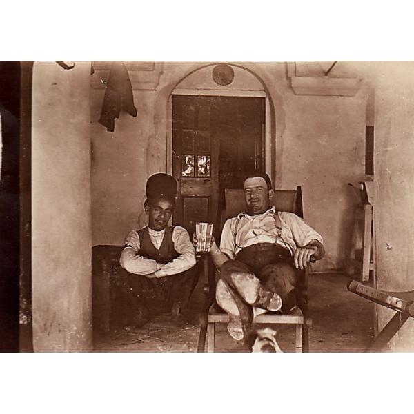 A photo of Humphrey Tracy laying back in a chair with a glass in his hand. There is a boy squatting beside him. 