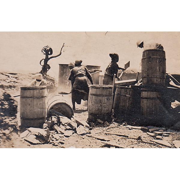 Five people surrounded by barrels and shoveling cement to build up a well. 