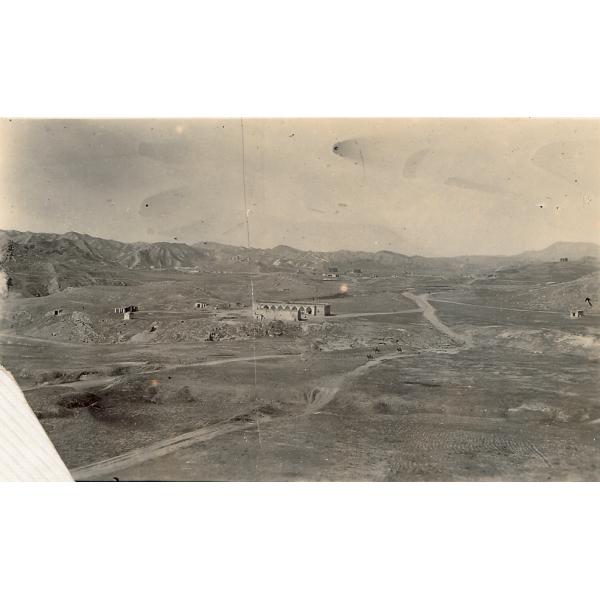 Une photo d’une route sillonnant le désert, avec des collines en arrière-plan. Il y a un bâtiment au centre de la photo. 