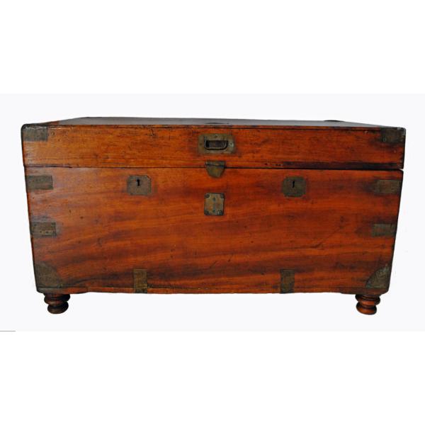 The front of a smooth wooden chest with a reddish hue. There are pieces of brass on the corners. The lock is also made of brass. There are circular legs on the bottom.