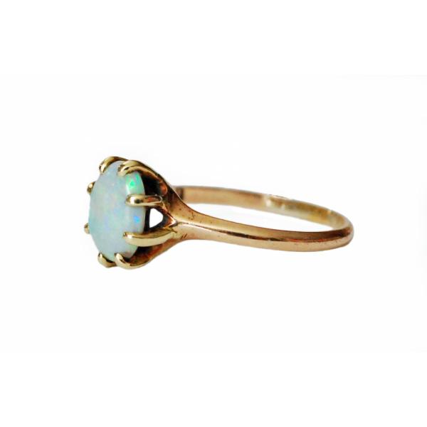 A green and blue stone set into a ring with eight gold prongs and a gold band, seen from the side. There are scratches on the band.