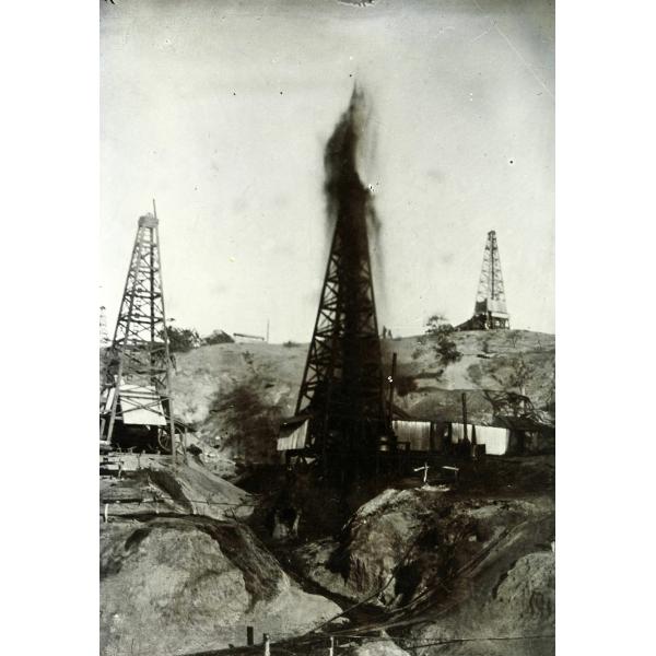 Three oil rigs on a hill. There is black oil gushing from the rig in the centre.