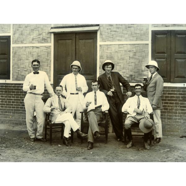 A photo of seven International Drillers, four standing and three seated in chairs. They are wearing suits or dress shirts.