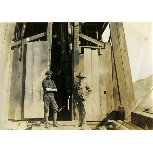 Two men wearing dark clothing standing in front of an opening in a rig covered with wooden planks.