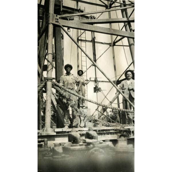 An International Driller and two local workers standing underneath an oil rig.