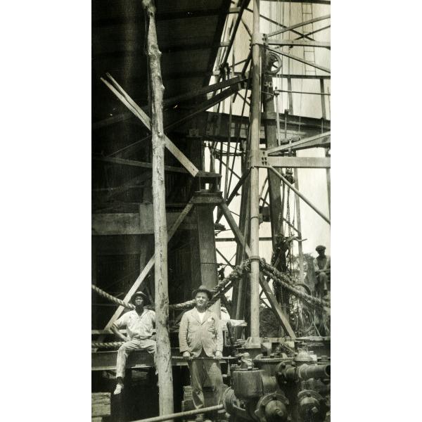 An International Driller and two local workers standing underneath an oil rig.