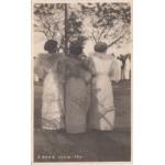 Front of a postcard showing the backs of three women in traditional dress.