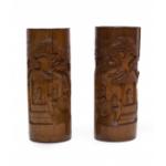 Two carved brown wooden vases. There are images carved into the vases of three bearded men standing near a roofed structure with a tree in the background. The relief images on the vases are mirror images of each other.