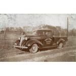 A two-door truck parked on the side of a dirt road with a field and trees in behind it. The truck is dark and has "Stover and Rawlings. Oil & Gas Well Contractors. Chatham" written on the door. 