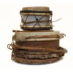 Two stacked drums from the side. Skins have been stretched across the tops and they are head together with string or hemp.