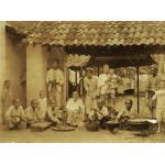 A group of people under an open structure with a tiled roof. There are boards and bowls in front of them and they are preparing food. 