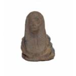 The front of a human-headed scarab made of brown clay. A face and headdress have been carved into the figure.