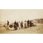 A photo of seven Egyptian men standing with a white woman a desert. There are two camels with saddles on their backs sitting in front of them.