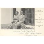 Vola and John Braybrook sitting on a windowsill. There are bars on the window and flowers by their feet. The photo is part of a Christmas card. 