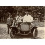 William McRae sitting in a car with a local man at the wheel. Another man stands to the side.  