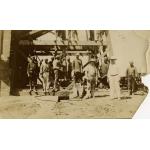 Photo d'un groupe d'hommes debout devant la base d'une tour de forage en bois. Il y a deux foreurs internationaux debout à l'avant, portant des tenues blanches et des casques coloniaux.