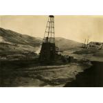 A photo of an oil rig with four legs on a dirt hill. The bottom part has been covered in dark cloth. There are piles of casing around the sides of the rig.