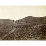 Photo d'un groupe d'hommes portant des paniers en équilibre sur la tête, marchant le long d'une route en pierre. Campbell se tient vers l’avant avec un autre homme.