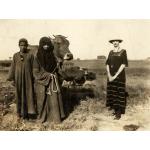 Une photo d'Annie Dyke debout à côté d'un garçon et d'une femme tenant une vache. Annie porte une robe à rayures foncées, la femme une robe foncée et un couvre-chef, et le garçon une robe foncée. Un champ se trouve derrière eux.  