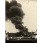 A photo of a group of people watching a cloud of black smoke near a group of oil derricks.