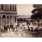 A photo of a crowded street outside of a large building near the waterfront.  