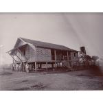 Bungalow in Myanmar, sitting on stilts with woven walls and a thatched roof. There are seven people and a horse standing outside. 